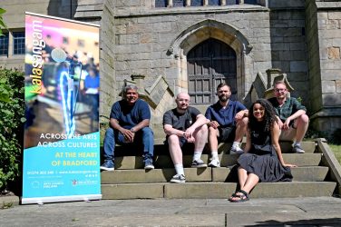 4 men and 1 women pose on steps in front of Bradford Cathedral, with a Kala Sangam banner to one side