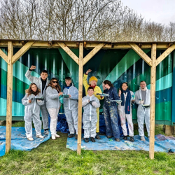 a group photo of 9 artists smiling in front of a mural