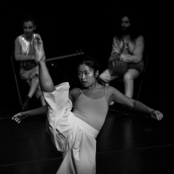 a female dancer with her leg in the air with two musicians behind her