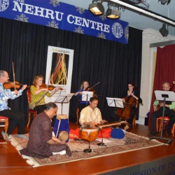 A picture of musicians sat on a stage playing various drums, violins and flutes