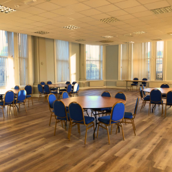 A room with lots of tables and chairs set up around the room with big floor length windows
