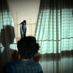 A woman standing still with her head down infront of a wall of mirrors and curtains